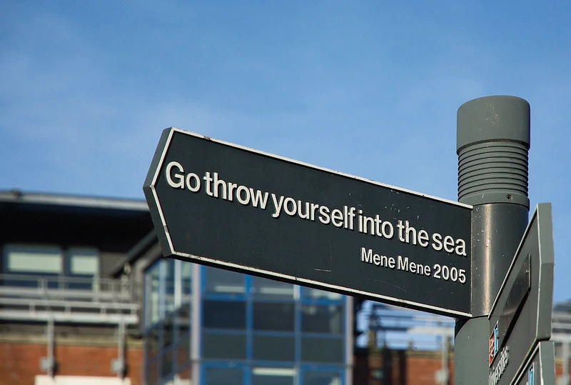 Photograph of a directional signpost reading:
Go throw yourself into the sea
Mene Mene 2005