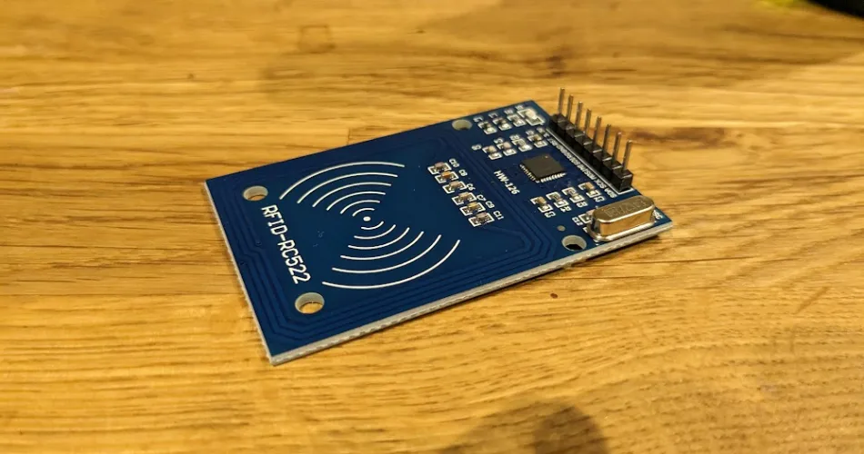 RC522 RFID module, a blue circuit board with a row of header pins and prominent wave markings where the antenna is located.